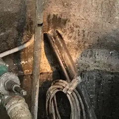 Rohrleitungen und Kabel in einem feuchten Bereich, der auf eine notwendige **Brunnenabdichtung** hindeutet.