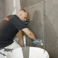 Bauarbeiter trägt Mörtel auf eine Wand auf, die mit Armierungsgewebe nach DIN EN 13670 versehen ist.