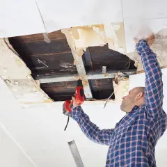 Mann repariert Decke nach kleinem Wasserschaden. Trocknung und Reparatur sind im Gange.