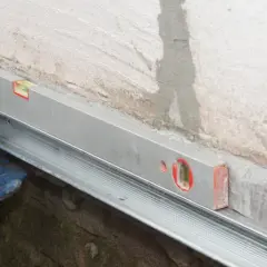 Handwerker montieren mit Wasserwaage und Bohrmaschine eine Horizontalsperre aus Blech an einer Wand.
