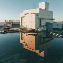 Flachdach mit Wasserpfützen, die ein Gebäude und Lüftungsanlagen spiegeln. Möglicherweise Anzeichen von Flachdach Blasenbildung unter der Oberfläche.