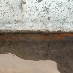 Wasser steht auf der Bodenplatte, ein Zeichen für einen hohen Grundwasserspiegel. Rostige Spuren deuten auf Feuchtigkeit hin.