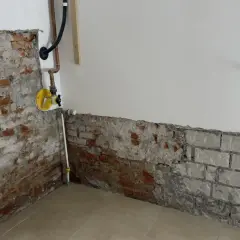 Baustelle mit freiliegendem Mauerwerk und Rohren. Ein gelbes Ventil deutet auf eine bevorstehende Maßnahme wie das Injektionsverfahren Horizontalsperre hin.