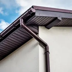 Braune Regenrinne und Fallrohr an der Traufe des Daches, bereit, Regenwasser abzuleiten.