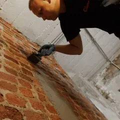 Mann mit Handschuhen trägt braune Wanne im Keller auf Ziegelwand auf.
