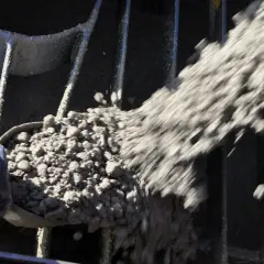 Beton wird mit einer Schaufel durch ein Gitter gegossen, das den Anforderungen der DIN EN 196-1 entspricht.