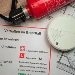 Brandschutz-Checkliste mit Feuerlöscher, Rauchmelder und Grundriss. Die Brandlast-Definition wird durch die gezeigten Elemente zur Brandverhütung verdeutlicht.