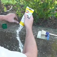 Hände dichten Betonrisse mit einer Tube ab. Ein Spachtel und Pinsel liegen bereit.