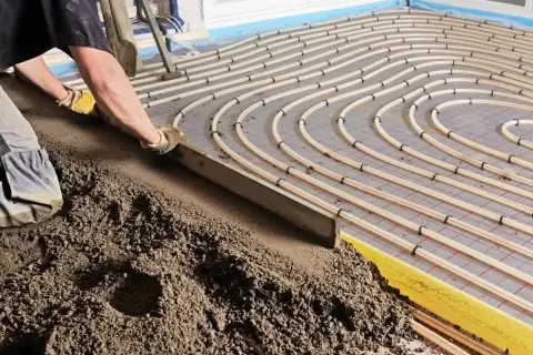 Arbeiter verlegt Estrich auf Fußbodenheizung, die den Normen nach DIN EN 13813 entspricht.