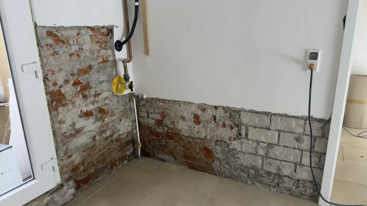 Baustelle mit freiliegendem Mauerwerk und Rohren. Ein gelbes Ventil deutet auf eine bevorstehende Maßnahme wie das Injektionsverfahren Horizontalsperre hin.