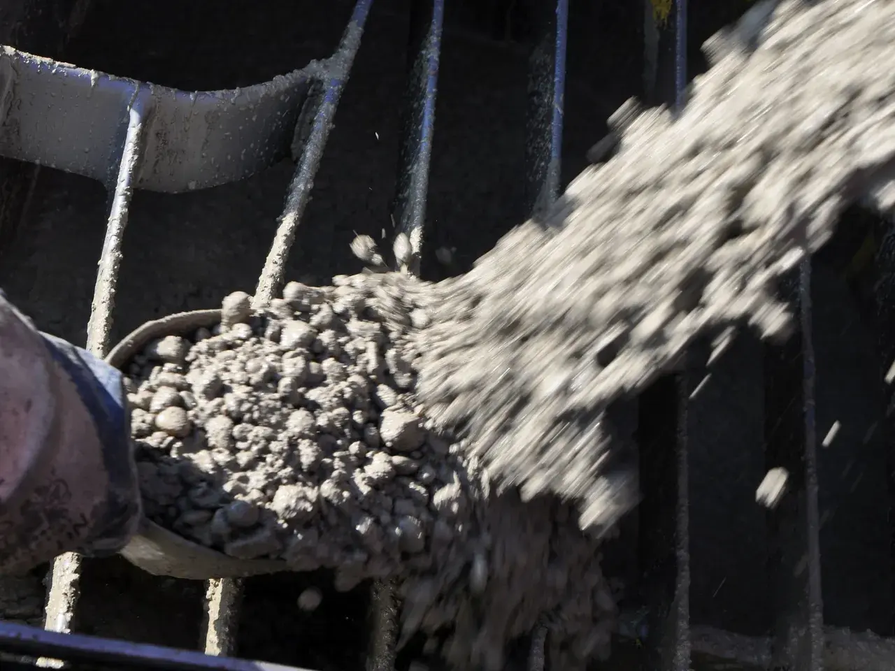 Beton wird mit einer Schaufel durch ein Gitter gegossen, das den Anforderungen der DIN EN 196-1 entspricht.