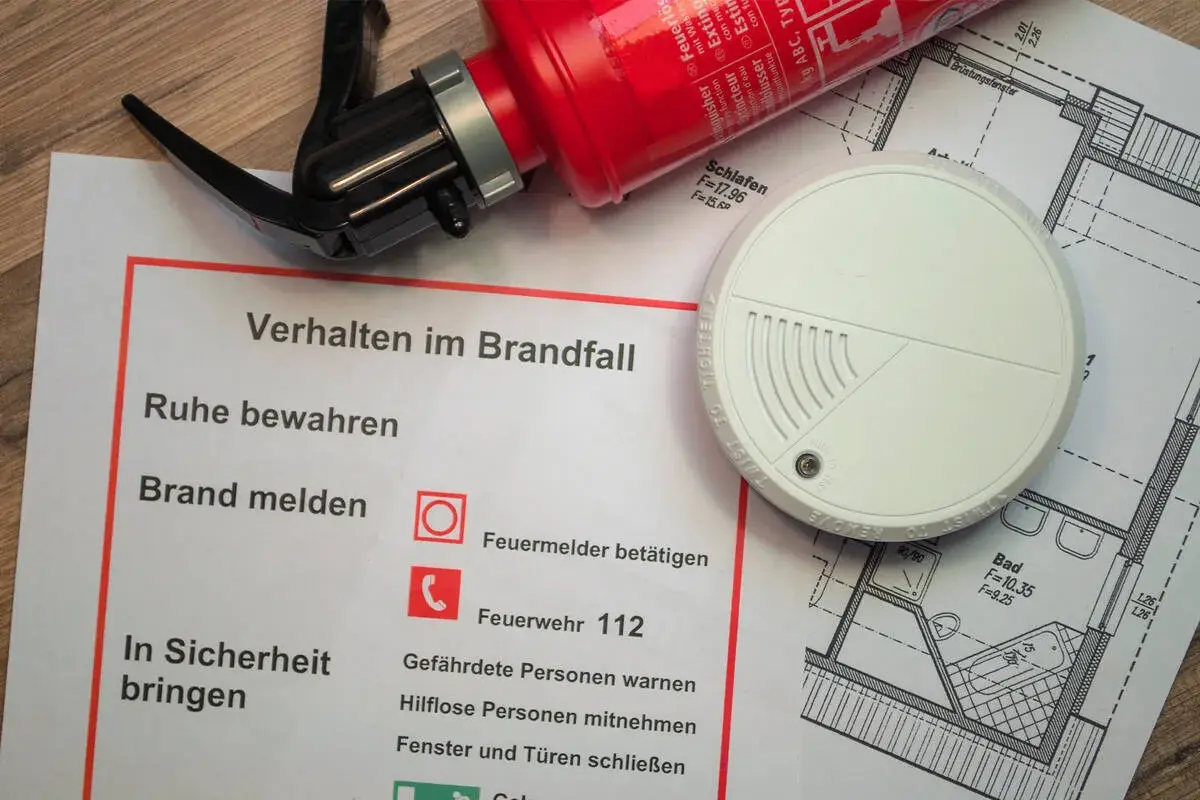 Brandschutz-Checkliste mit Feuerlöscher, Rauchmelder und Grundriss. Die Brandlast-Definition wird durch die gezeigten Elemente zur Brandverhütung verdeutlicht.