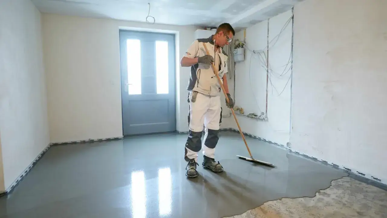 Ein Mann verteilt mit einem Rakel feuchten Boden in einem Raum. Der Boden glänzt nass.