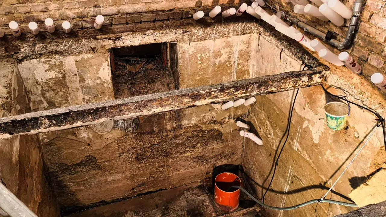 Arbeiten am Naturkeller Boden sanieren: Feuchte Wände, Rohre und ein Eimer deuten auf eine Baustelle hin.